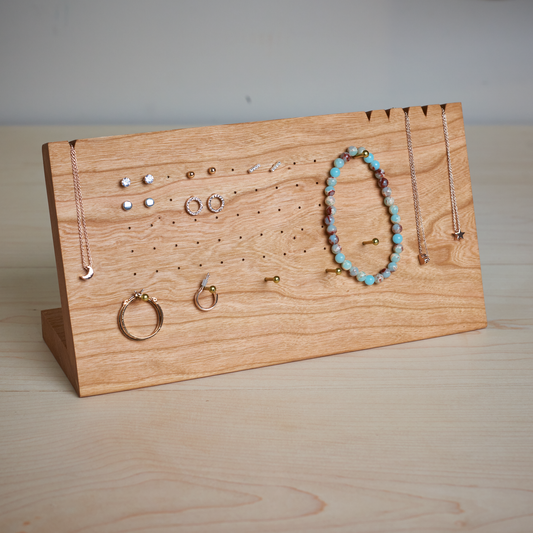 A handcrafted cherry wood jewelry stand with various earrings, rings, bracelets, and necklaces displayed on it.
