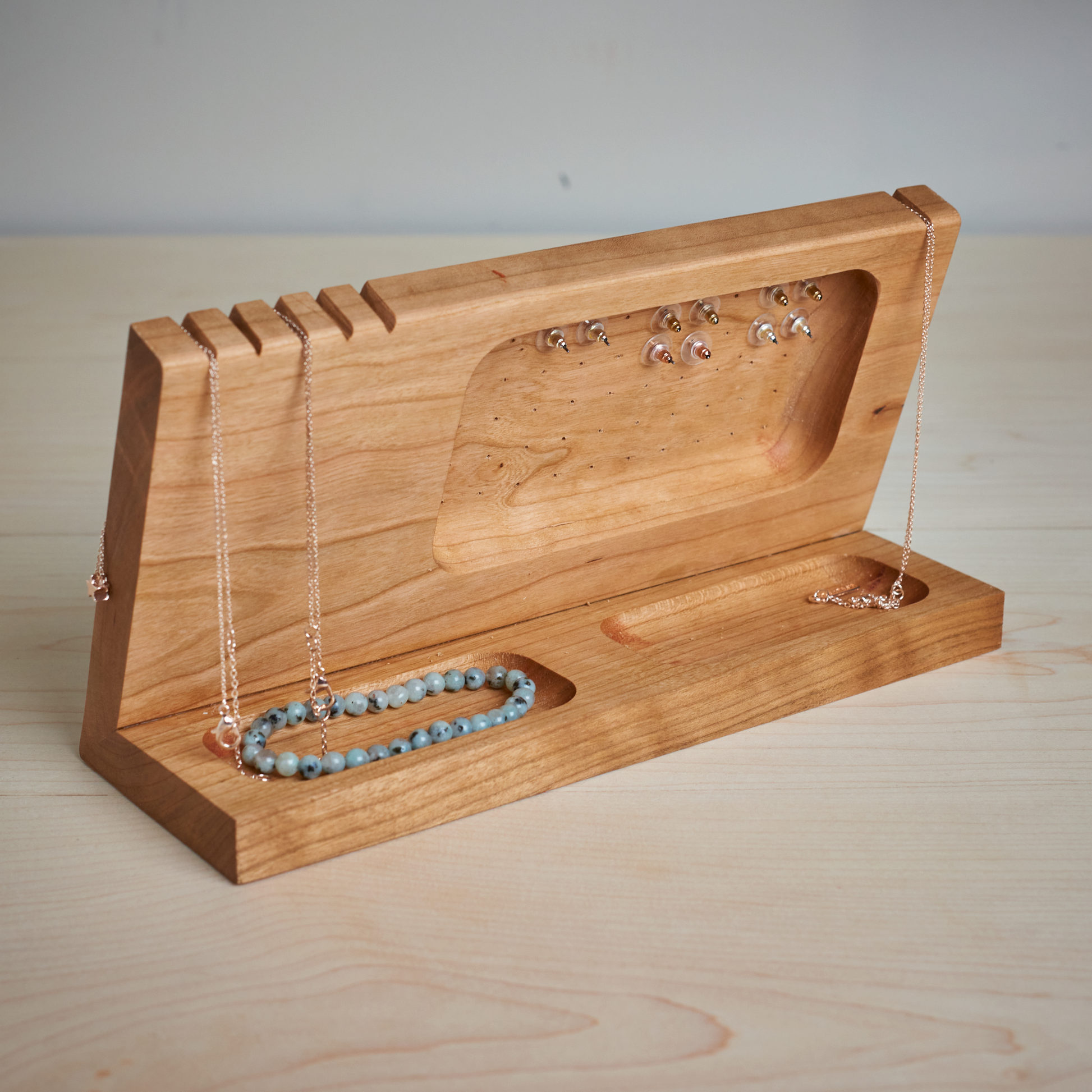 A handcrafted cherry wood jewelry stand with various earrings, rings, bracelets, and necklaces displayed on it.